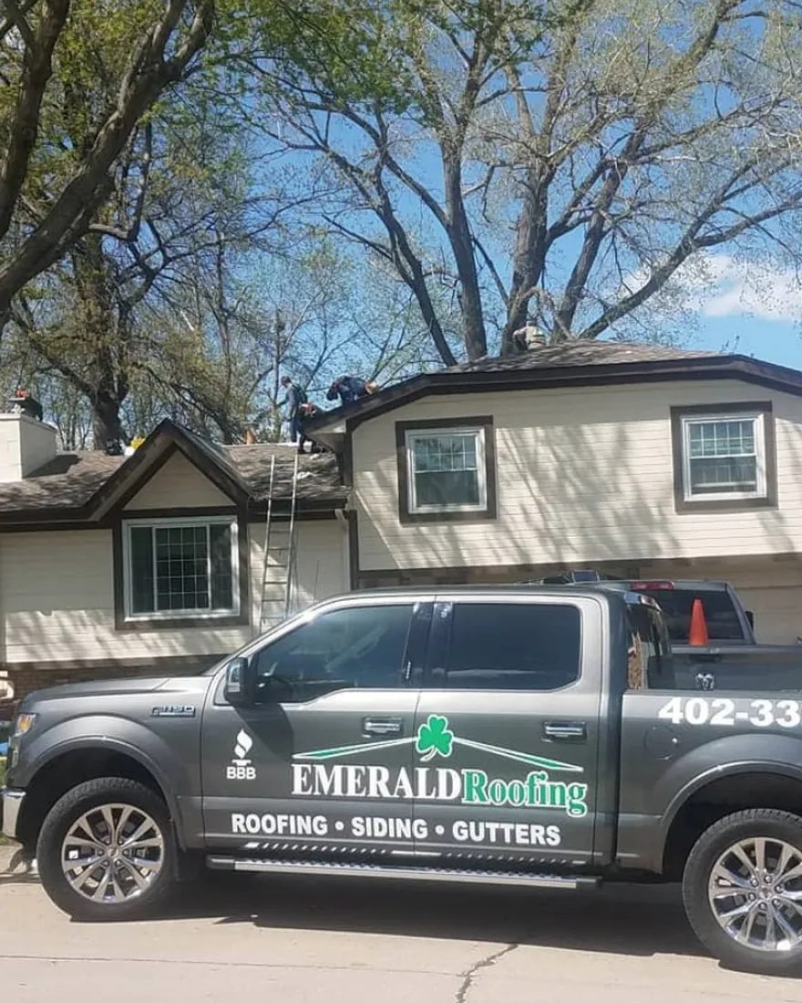 Emerald Exteriors crew on site — truck out front, ladder up, crew on the roof